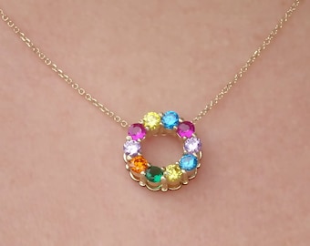 May include: A gold-colored necklace featuring a circular pendant adorned with a vibrant array of colorful gemstones. The gemstones are arranged in a circle, showcasing a spectrum of colors. The necklace is displayed against a white background.