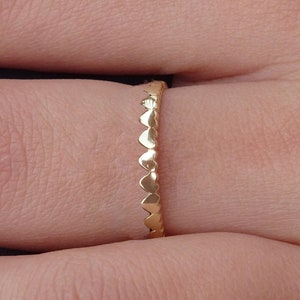 Könnte beinhalten: Ein goldener Ring mit einem herzförmigen Design. Der Ring ist dünn und zart, und die Herzen sind gleichmäßig um das Band verteilt.