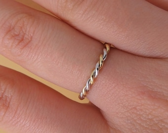 May include: A delicate ring with a twisted design, featuring alternating strands of gold, silver, and gold. The ring is shown on a finger, highlighting its intricate detail and the contrast of the metals.