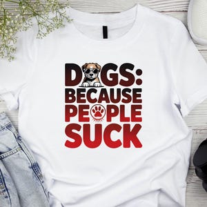 May include: White t-shirt with the text "DOGS: BECAUSE PEOPLE SUCK" in black and red. The word "DOGS" has a dog wearing sunglasses as the letter "O". A paw print is in the word "PEOPLE".