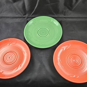 May include: Three ceramic plates, two red and one green, with a concentric circle design. The plates are all the same size and have a slightly raised rim.