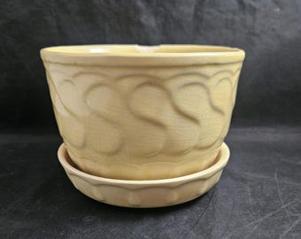 May include: A yellow ceramic planter with a scalloped rim and a matching saucer. The planter has a textured design of overlapping leaves.