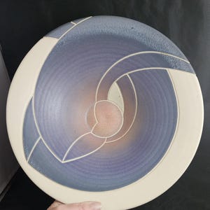 May include: A large, round ceramic bowl with a white rim and a blue and purple glaze. The bowl has a geometric design carved into the surface.