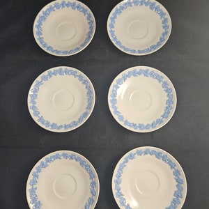 May include: Six white ceramic saucers with a blue floral pattern around the edge. The saucers are arranged in two rows of three.