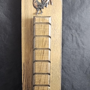 May include: Wooden rooster-themed key holder. The rectangular board has a carved rooster at the top and a series of slots below. Three pegs are at the bottom. The wood has a light brown finish.