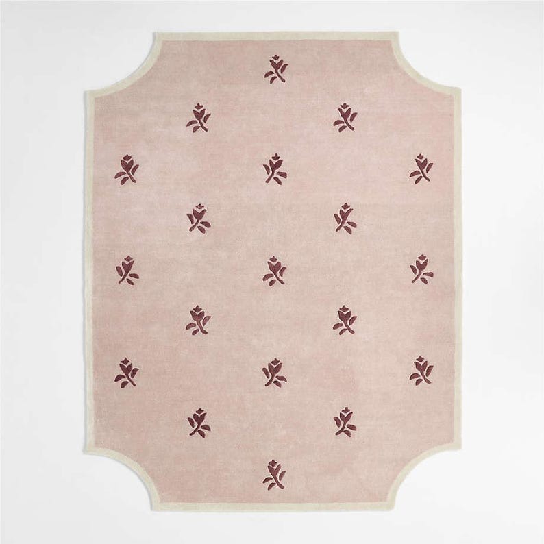 Puede incluir: Una alfombra rectangular con fondo rosa claro y borde crema. La alfombra presenta un patr&oacute;n repetido de motivos florales rojo oscuro. La forma de la alfombra tiene un borde decorativo y curvado.