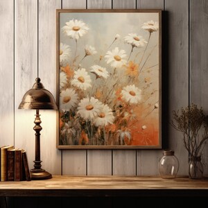 May include: A framed painting of white daisies with orange accents on a light brown wood background. The painting is hanging on a wall with a lamp and books on a table below.