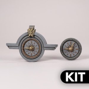 Könnte beinhalten: Ein Set aus grauen und messingfarbenen mechanischen Uhrkomponenten, bestehend aus einem größeren kreisförmigen Teil mit seitlichen Verlängerungen und einem kleineren kreisförmigen Teil. Beide haben ein Zifferblatt mit Zeigern und einen Perlenrand. Das Wort KIT ist in Weiß gedruckt.