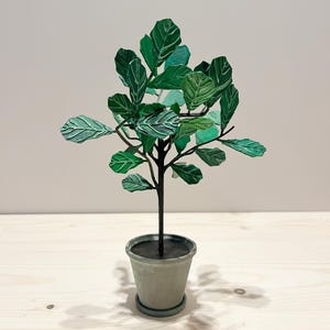 May include: A miniature decorative potted plant with large, textured green leaves. The plant has a dark brown stem and is set in a grey pot with a matching saucer. The plant is a miniature version of a fiddle-leaf fig tree.