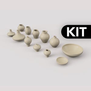 Könnte beinhalten: Eine Sammlung kleiner, hellbeiger Keramikgefäße, bestehend aus verschiedenen abgerundeten Vasen, einer Schale und einem flachen Teller, angeordnet auf einer schlichten Oberfläche. Das Wort KIT steht in weißer Schrift auf schwarzem Grund oben rechts.