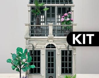 以下が含まれることがあります： グレーと白のファサード、鉢植えの植物と緑の屋根が付いたバルコニーを備えた、2階建てのミニチュアのドールハウスキット。 キットには、ミニチュアの植物とアクセサリーが含まれています。 「KIT」という単語が黒い背景に白で表示されています。