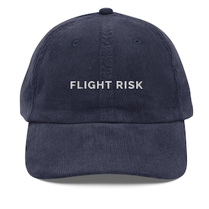 May include: A navy blue corduroy baseball cap with white embroidered text that reads "FLIGHT RISK".
