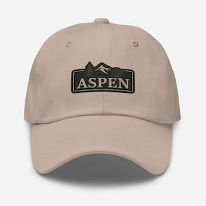 Könnte beinhalten: Eine beige Dad Cap mit einem gestickten Aufnäher, auf dem "ASPEN" in weißen Buchstaben steht. Der Aufnäher zeigt eine grüne Bergkette und ein grünes Blatt.