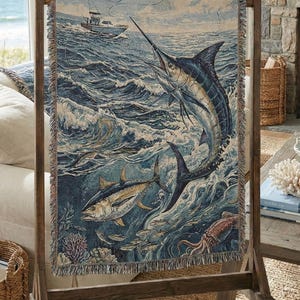 May include: A woven tapestry featuring a marine scene with a marlin leaping from the ocean, a tuna, and a boat in the distance. The tapestry is displayed on a wooden stand, showcasing a nautical theme with shades of blue, beige, and brown.