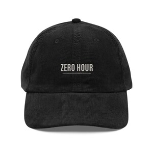 Peut inclure: Casquette de baseball en velours côtelé noir avec le texte "ZERO HOUR" en blanc. La casquette a une visière incurvée et une couronne arrondie. Le chapeau est de couleur noire unie.