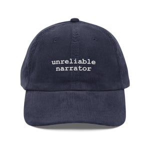 Puede incluir: Una gorra de béisbol de pana azul marino con texto bordado en blanco que dice "narrador poco fiable".