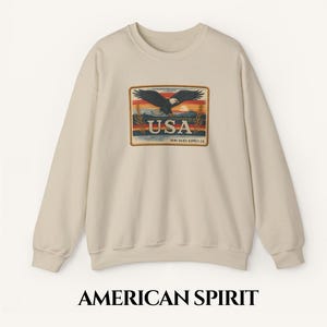 Könnte beinhalten: Ein beiger Pullover mit einem Vintage-Grafikdruck eines Adlers, der über einem Sonnenuntergang fliegt, mit dem Text "USA" und "TENN. SKIES SUPPLY CO."