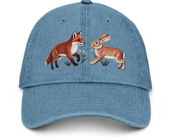 Könnte beinhalten: Eine blaue Denim-Baseballkappe mit einem gestickten Bild eines Fuchses und eines Kaninchens. Der Fuchs ist orange und weiß, und das Kaninchen ist braun und weiß.