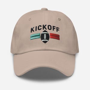 May include: A tan baseball cap with the text "KICKOFF" embroidered in black. The cap features a green, red, and white football graphic.