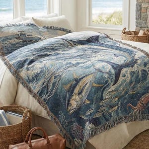 May include: A blue and white woven throw blanket featuring a marlin and other fish swimming in the ocean. The blanket has a fringed edge and is placed on a bed with matching pillow shams. The scene includes a fishing boat.