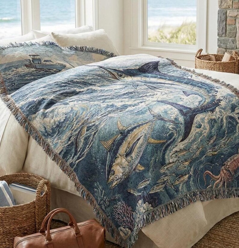 May include: A blue and white woven throw blanket featuring a marlin and other fish swimming in the ocean. The blanket has a fringed edge and is placed on a bed with matching pillow shams. The scene includes a fishing boat.