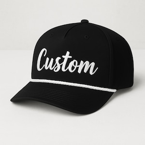 Peut inclure: Casquette de baseball noire avec le mot "Custom" brodé en blanc sur le devant. Un détail de corde blanche orne le bord. La casquette a une visière incurvée et un bouton sur le dessus.