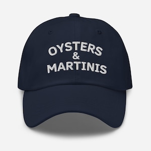 May include: A navy blue baseball cap with white embroidered text that reads "Oysters & Martinis".