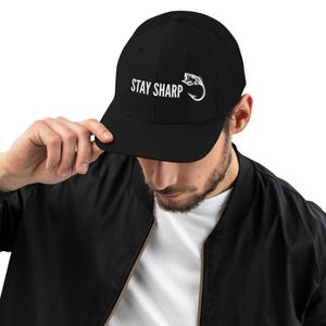 May include: Black mesh trucker hat with a white embroidered fish and the text "STAY SHARP".