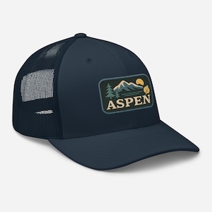 Könnte beinhalten: Eine marineblaue Trucker-Kappe mit schwarzem Netzrücken. Die Kappe hat einen Aufnäher mit einer Bergszene und dem Wort "ASPEN" in einer Vintage-Schriftart.
