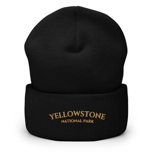 May include: Black beanie with the words "YELLOWSTONE NATIONAL PARK" embroidered in gold thread. The beanie is a classic, cuffed style, perfect for outdoor adventures or casual wear. The hat is made of a soft, knitted material.