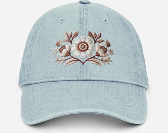 May include: A light blue denim baseball cap with an embroidered floral design in white and brown.