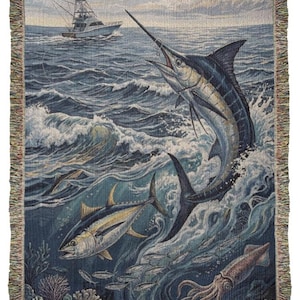 May include: Woven throw blanket featuring a marine scene with a marlin leaping from the ocean, a tuna, and a fishing boat. The blanket has a fringed edge and depicts a vibrant underwater world with shades of blue, green, and white.