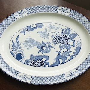 May include: A white oval platter with a blue and white floral design featuring a bird with a long tail. The border of the platter has a repeating geometric pattern.