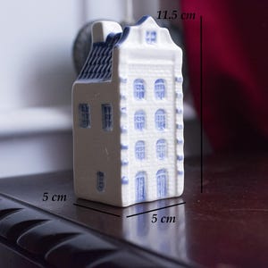 Puede incluir: Una casa en miniatura de cerámica blanca con bordes y ventanas azules. La casa mide 5 cm de ancho y 11,5 cm de alto.