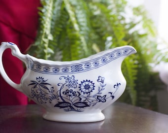 May include: A white gravy boat with a blue and white floral design. The boat has a wide, rounded base and a spout on one side.