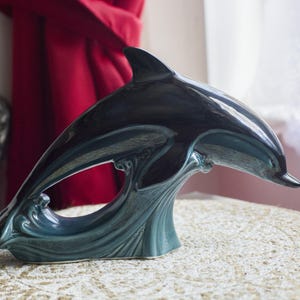 May include: A teal blue ceramic dolphin figurine leaping out of the water. The dolphin is glazed with a shiny finish.