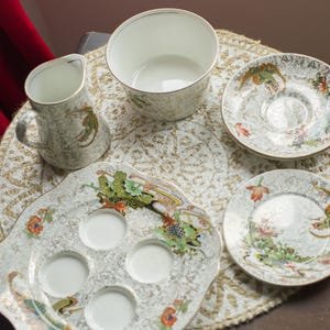 Peut inclure: Un ensemble de tasses à thé et de soucoupes vintage avec un motif floral. Les tasses et les soucoupes sont blanches avec une bordure dorée et présentent un délicat motif floral dans des tons de vert, rose et bleu. L'ensemble comprend un pot à crème, un sucrier et une petite assiette avec six tasses individuelles.
