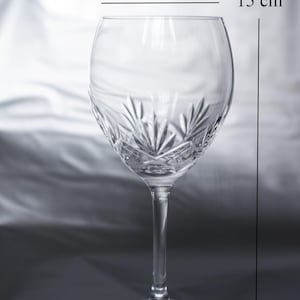 May include: A clear crystal wine glass with a decorative etched pattern on the bowl. The glass is 15 cm tall, with a bowl diameter of 5.6 cm and a base diameter of 6.5 cm. The stem is slender, and the base is round.