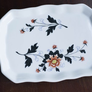 May include: White ceramic serving tray with a scalloped edge and a floral design in black, brown, and blue.