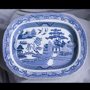 May include: Oval blue and white ceramic serving platter with a detailed Willow pattern design. The platter features a central landscape scene with pagodas, bridges, and birds, surrounded by a decorative border. The platter measures approximately 40 cm in length.