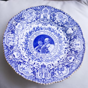 May include: A blue and white commemorative plate with a portrait of King Edward VII and Queen Alexandra. The plate has a detailed floral and crest design around the rim and a gold trim. The text reads "EDWARD VII. KING. ALEXANDRA QUEEN. JUNE 26 CORONATION 1902."
