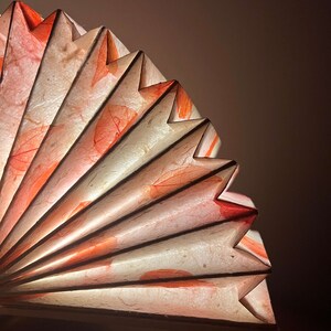 May include: A white paper fan with red leaf designs. The fan is folded and has a delicate, intricate design.