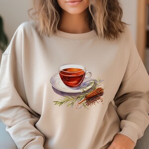 May include: A beige sweatshirt with a graphic of a cup of tea, cinnamon sticks, and rosemary sprigs.