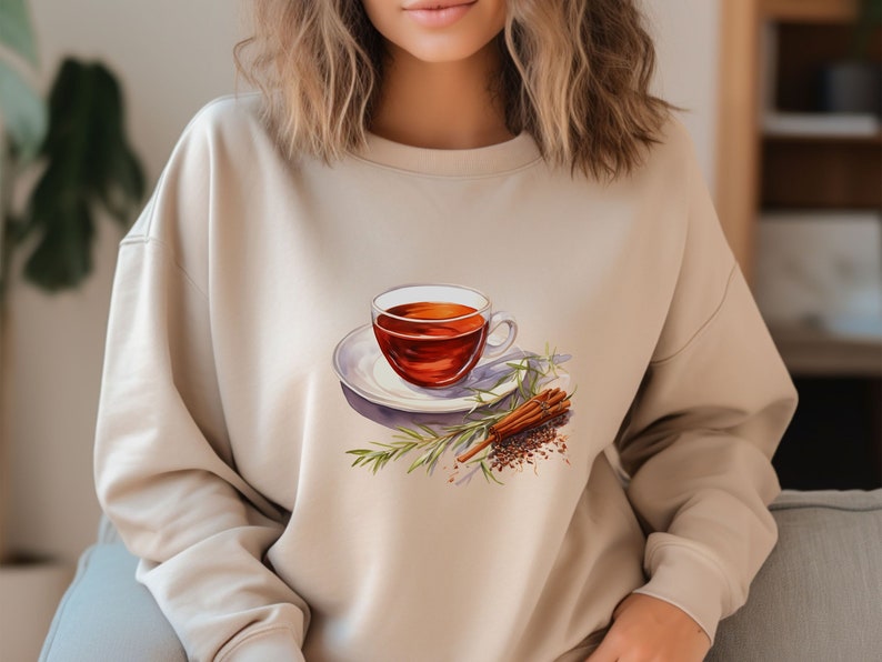 May include: A beige sweatshirt with a graphic of a cup of tea, cinnamon sticks, and rosemary sprigs.