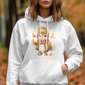 May include: White hoodie with a cute cartoon squirrel wearing a brown jacket and a red scarf. The squirrel is surrounded by falling autumn leaves.