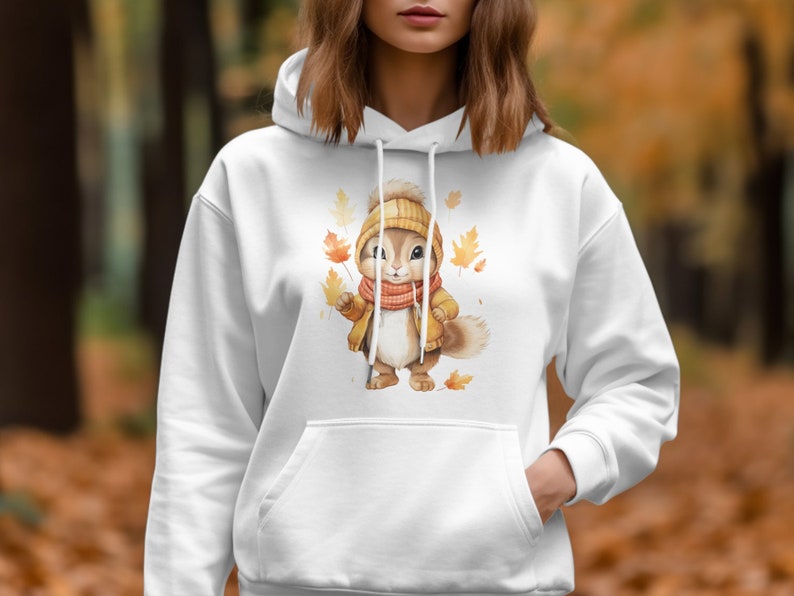 May include: White hoodie with a cute cartoon squirrel wearing a brown jacket and a red scarf. The squirrel is surrounded by falling autumn leaves.