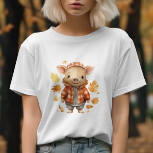 May include: White t-shirt with a cartoon pig wearing a red and black plaid jacket and a brown hat. The pig is surrounded by orange and brown leaves.