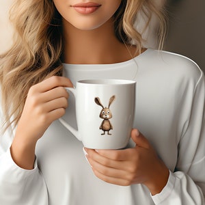 May include: White ceramic mug featuring a brown cartoon bunny illustration. The bunny has large ears, brown fur, and a white face.