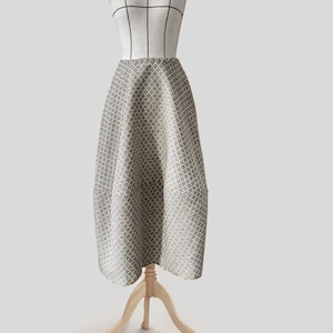 Peut inclure: Une longue jupe fluide avec un motif géométrique dans les tons de gris et de blanc. La jupe est présentée sur un mannequin.