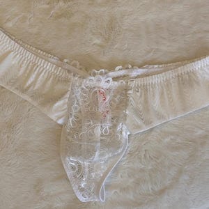 Puede incluir: Lencería blanca con un delicado panel frontal de encaje. La ropa interior presenta un diseño de talle bajo y está hecha de una tela suave estampada. Los detalles de encaje añaden un toque de elegancia.
